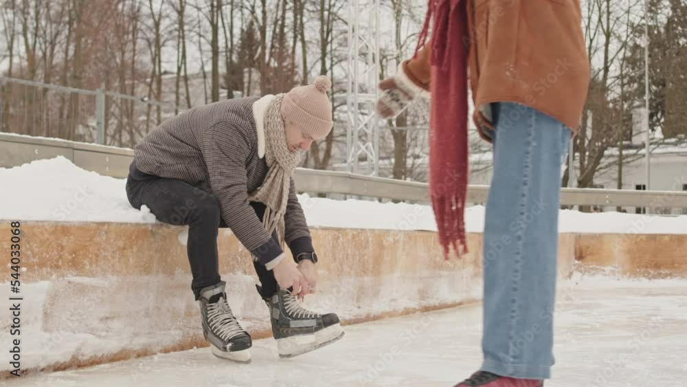 Young cheerful couple wearing skates holding hands while ice skating on rink outdoors on winter holidays Young cheerful couple wearing skates holding hands while ice skating on rink outdoors on winter holidays