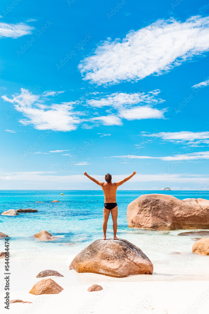 Happy man on the beautiful sandy beach rising hands to the sky on summer vacations on Seychelles. Freedom and happiness concept