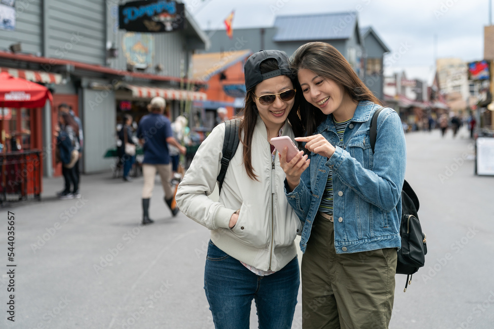 people on vacation in usa. asian woman tourist pointing at fun places to visit as she is checking travel info on the phone with her girl partner on the street at Old Fisherman's Wharf people on vacation in usa. asian woman tourist pointing at fun places to visit as she is checking travel info on the phone with her girl partner on the street at Old Fisherman's Wharf