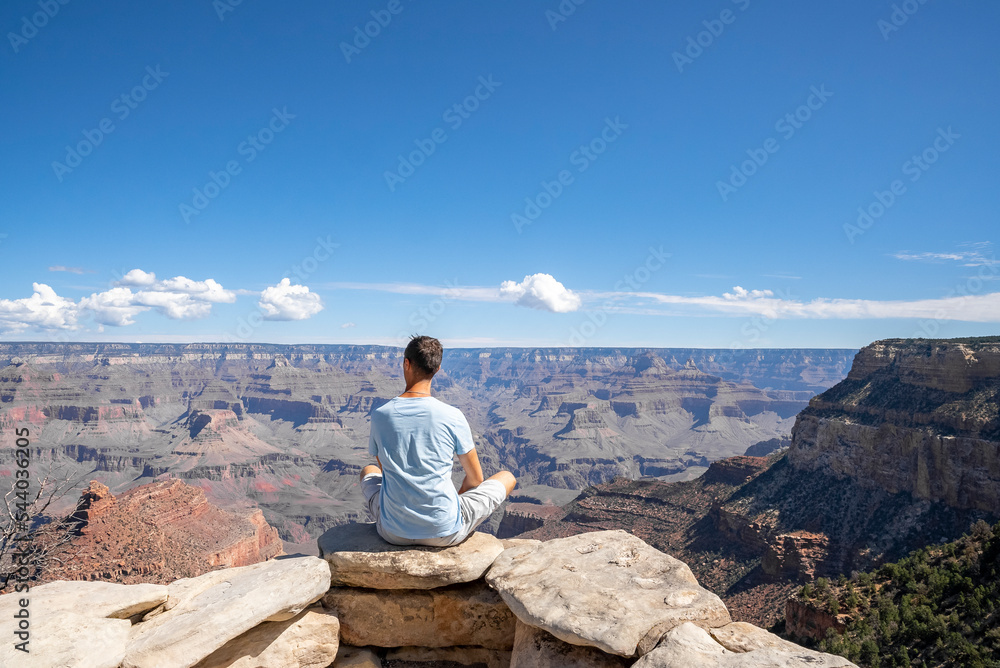 Rear View Of Man Sitting On Viewpoint And Exploring Scenic Grand Canyon National Park During Sunny Day At Arizona