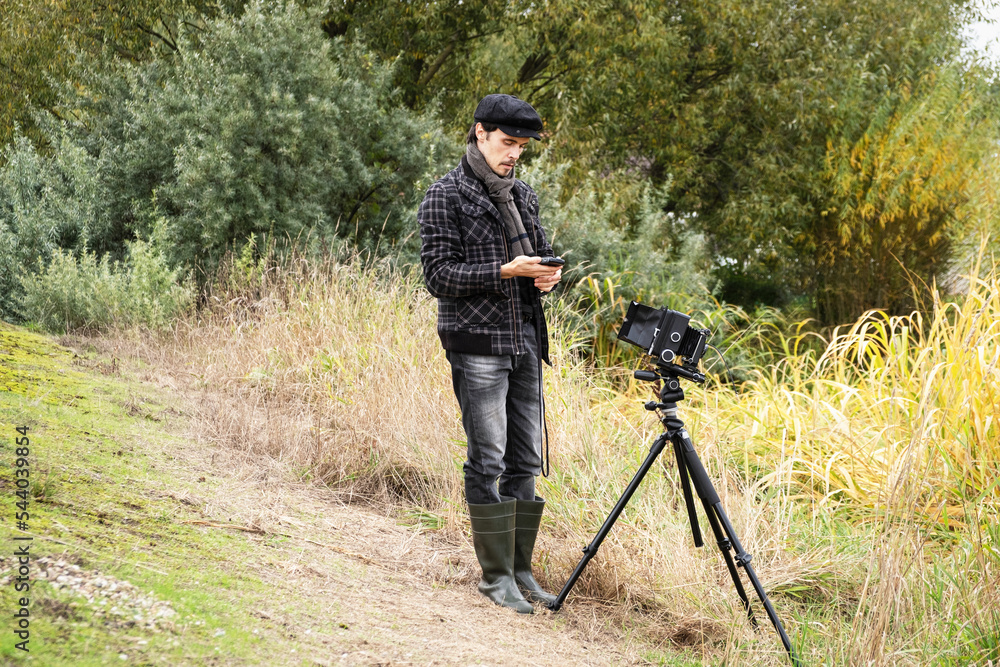 Photographer in the process of shooting on large-format retro camera. Shooting an autumn landscape with an old camera. Concept - old classic process, film camera.