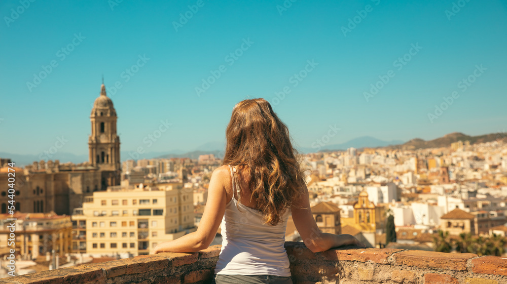 Malaga- Woman standing on the balcony, looking at panoramic cityscape view- Andalusia, Spain