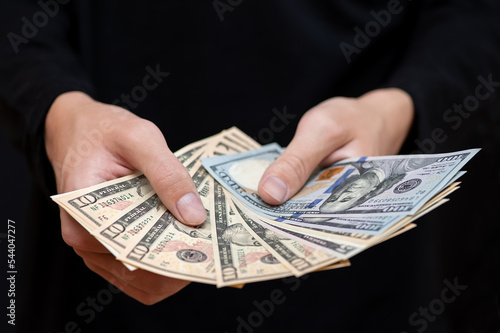 Different dollar bills in the hands of a young man in dark clothes, close-up.