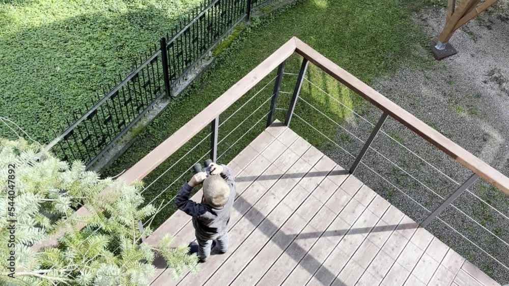 A boy with binoculars in his hands stands on the terrace and observes nature A boy with binoculars in his hands stands on the terrace and observes nature
