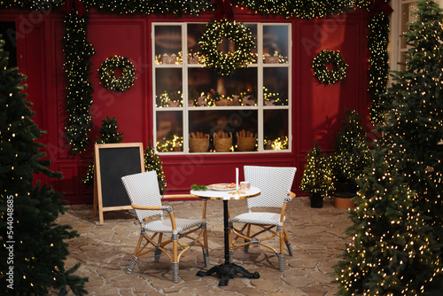 Table for two. Christmas cafe exterior with Christmas decorations and fresh bread in glass showcase. Cozy outdoor cafe on Christmas eve. Copy space. seasonal greetings concepts. Red walls
