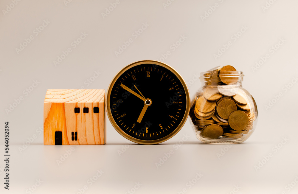 Golden alarm clock, model wooden house and silver gray background, coin saving ideas to build a home and personal business for a sustainable future. Golden alarm clock, model wooden house and silver gray background, coin saving ideas to build a home and personal business for a sustainable future.