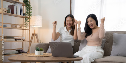 Exciting young asian women LGBT lesbian happy couple sitting on sofa using laptop a computer and phone in living room at home. LGBT lesbian couple together