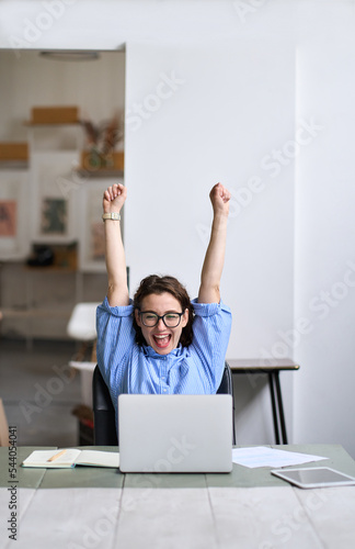 Fotografía Young happy business woman office worker student feeling excited raising hands winning online looking at laptop celebrating professional achievement, good online result getting hired approved at work