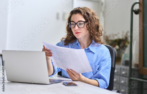 Foto Young busy business woman manager, lawyer or company employee holding accounting bookkeeping documents checking financial data or marketing report working in office with laptop