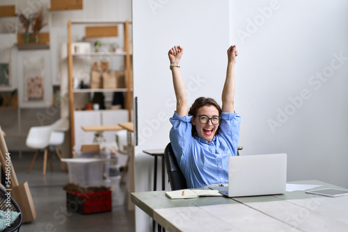 Happy excited young woman student or employee, office worker winner using laptop computer celebrating goal achievement winning online getting good news in email raising hands feeling euphoric. photo