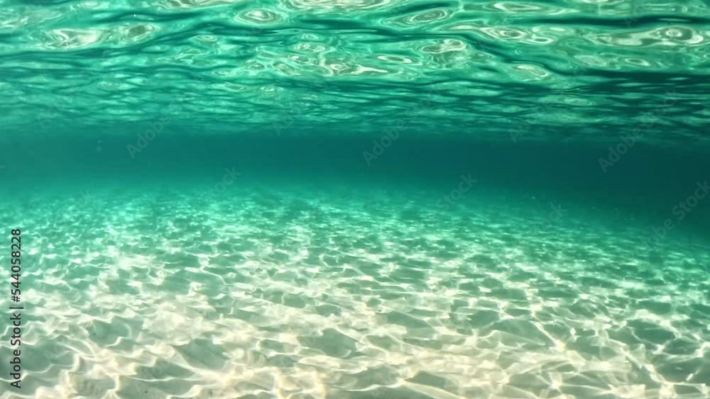 Sandy beach and sea bottom in sunny day. Rays of the sun make their way through the sea water forming bizarre patterns on the sandy bottom. Underwater shot, slow motion Sandy beach and sea bottom in sunny day. Rays of the sun make their way through the sea water forming bizarre patterns on the sandy bottom. Underwater shot, slow motion
