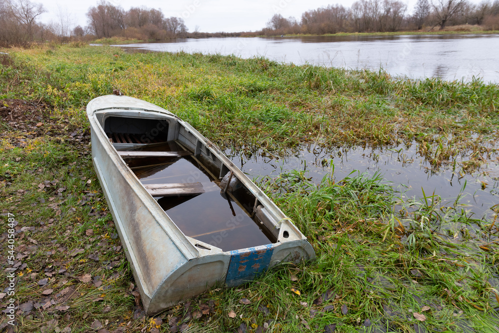 A semi-submerged aluminum or duralumin boat on a swampy river bank. Autumn, October. november. Overcast weather A semi-submerged aluminum or duralumin boat on a swampy river bank. Autumn, October. november. Overcast weather
