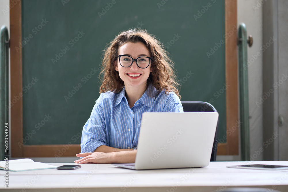 Young happy business woman sitting at work desk with laptop. Smiling school professional online teacher coach advertising virtual distance students classes teaching remote education training. Portrait Young happy business woman sitting at work desk with laptop. Smiling school professional online teacher coach advertising virtual distance students classes teaching remote education training. Portrait