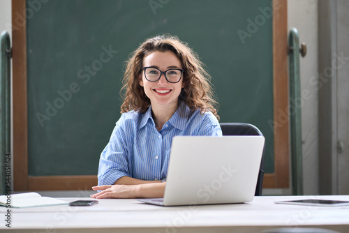 Young happy business woman sitting at work desk with laptop. Smiling school professional online teacher coach advertising virtual distance students classes teaching remote education training. Portrait photo