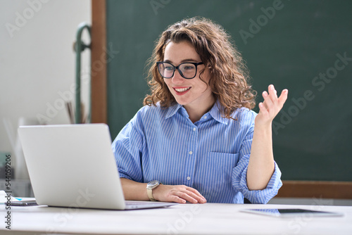 Young happy professional business woman online teacher or tutor sitting at work desk talking to student on video call teaching remote class, leading webinar or distance web meeting on laptop computer.