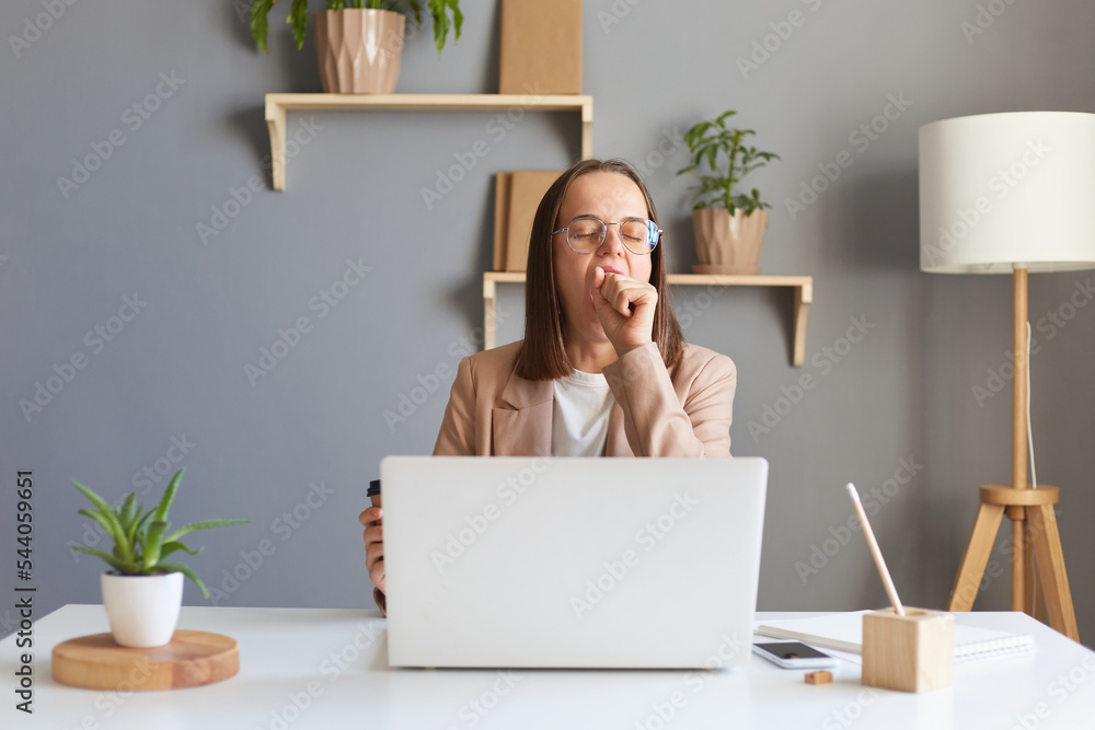 Αυτοκόλλητο Portrait of sleepless tired woman office manager with dark hair sitting at table and working on laptop, being exhausted, yawning, covering mouth with hand, being sleepy