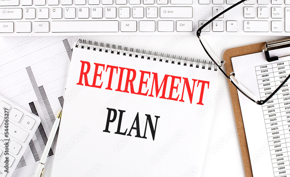 Text RETIREMENT PLAN on Office desk table with keyboard, notepad and analysis chart on white background. Text RETIREMENT PLAN on Office desk table with keyboard, notepad and analysis chart on white background.