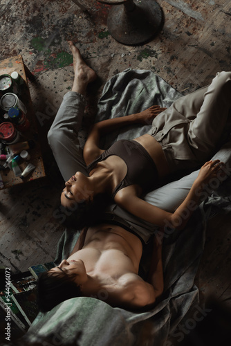 top view of passionate african american woman in top and pants lying with closed eyes near sexy man on floor in workshop.