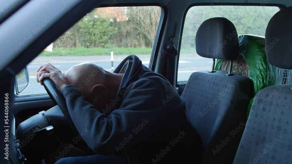 A mature man crying in his car at the side of the road with his head in his hands on the steering wheel