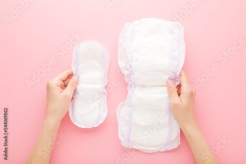 Young adult woman hands holding opened white sanitary towels on pink table background. Big and small size. Pastel color. Hygiene product for urinary incontinence or after childbirth. Top down view. photo