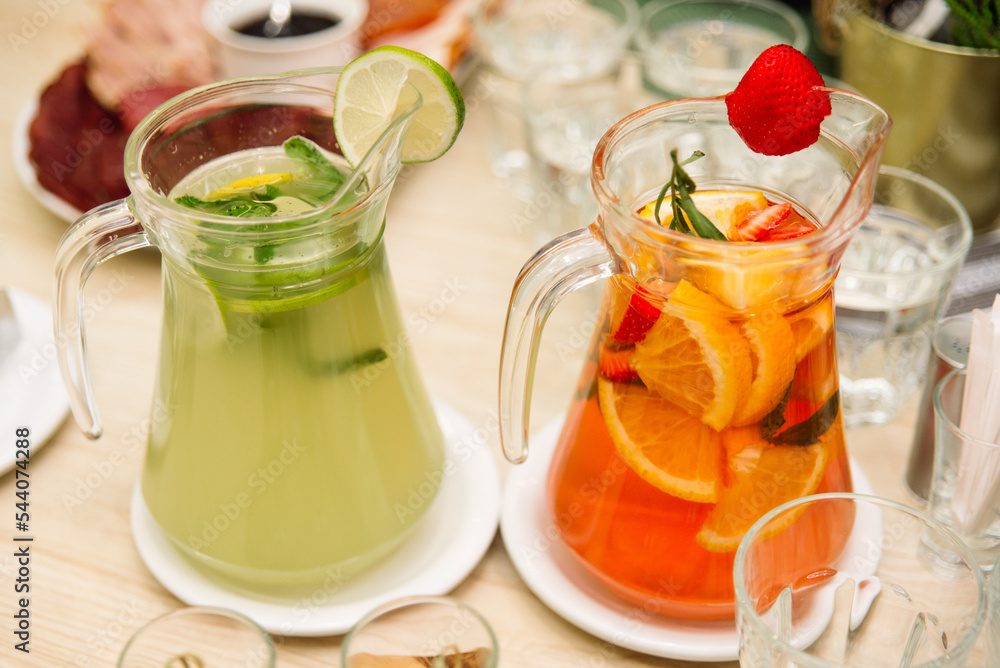 Fototapeta premium Citrus lemonades. Two pitchers of homemade lemonades. Lime slices, mint leaves, orange slices and strawberries.