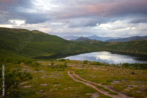 panorama of acre northern norway at sunrise, country road leading towards a lake surrounded by mighty mountains, vacation in the arctic