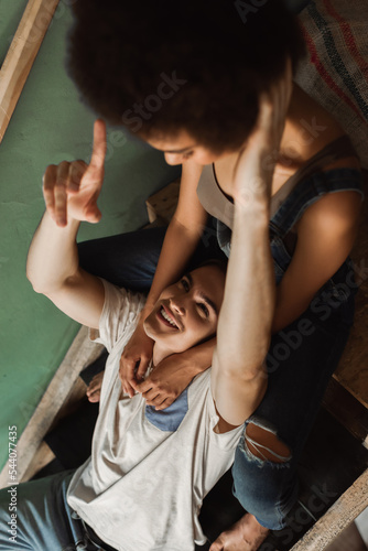 high angle view of cheerful man pointing with finger near blurred african american girlfriend on stairs in workshop.