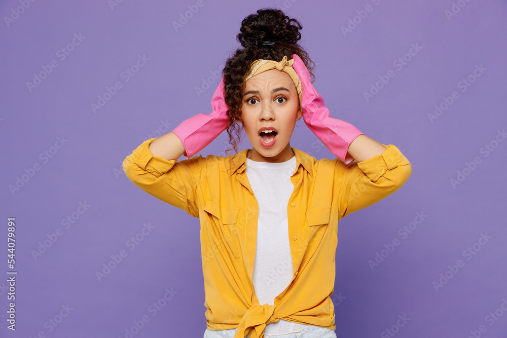 Young shocked scared amazed astonished sad woman wear yellow shirt rubber gloves while doing housework tidy up hold head isolated on plain pastel light purple background studio. Housekeeping concept. Young shocked scared amazed astonished sad woman wear yellow shirt rubber gloves while doing housework tidy up hold head isolated on plain pastel light purple background studio. Housekeeping concept.