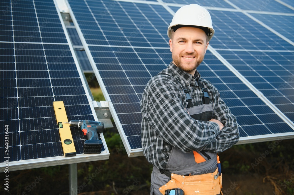 A handyman standing on the rooftop with solar panels and smiling at the camera. A handyman standing on the rooftop with solar panels and smiling at the camera.
