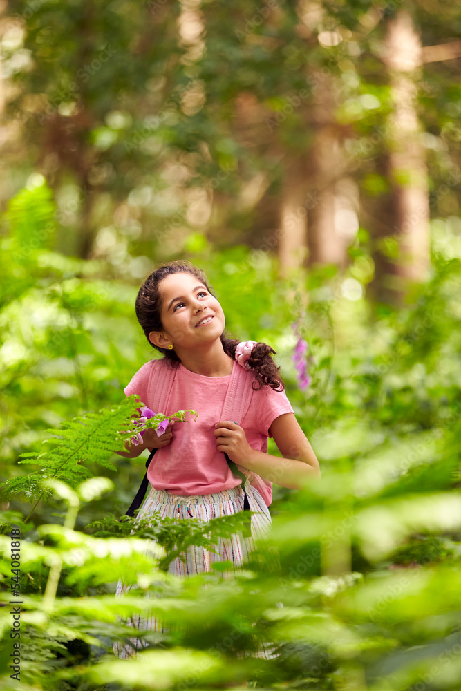 Smiling Girl Walking In Summer Woodland Surrounded By Ferns Wearing Backpack