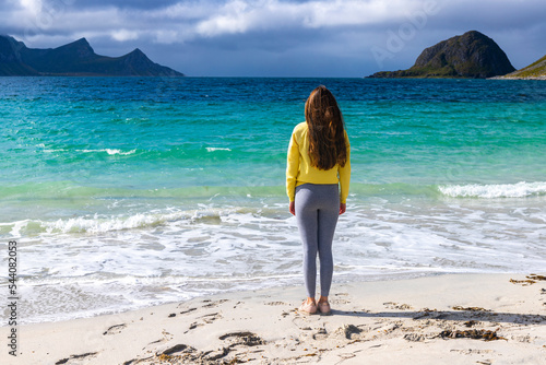 a beautiful long-haired girl enjoys the sunny weather on the famous paradise beach of haukland on the lofoten islands in northern norway  a beach walk in the norwegian fjords