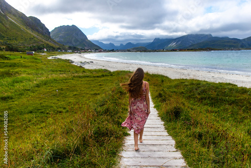 beautiful long-haired girl in a dress walks along the famous ramberg beach (rambergstranda) on the lofoten islands in northern norway; a beach holiday in the norwegian fjords photo