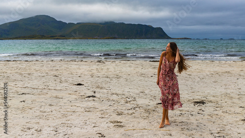 beautiful long-haired girl in a dress walks along the famous ramberg beach (rambergstranda) on the lofoten islands in northern norway; a beach holiday in the norwegian fjords