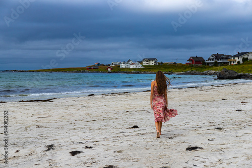 beautiful long-haired girl in a dress walks along the famous ramberg beach (rambergstranda) on the lofoten islands in northern norway; a beach holiday in the norwegian fjords photo