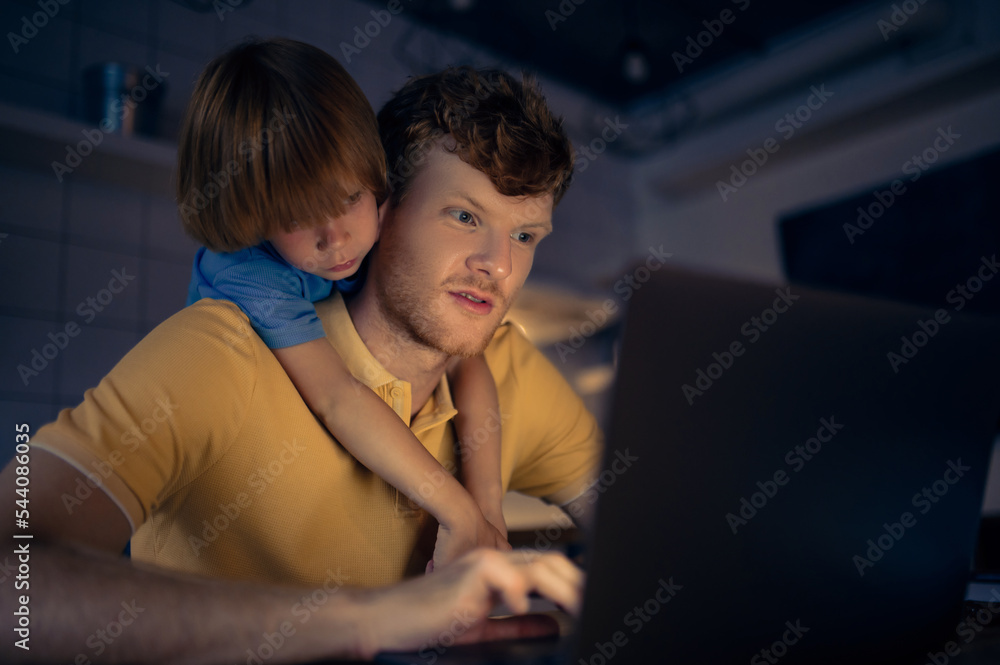 Ginger man nad his cute son watching something on internet in the evening Ginger man nad his cute son watching something on internet in the evening