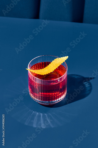 Popular cocktail negroni with gin and vermouth on blue background with shadow. Negroni cocktail on coloured background in trendy style. Contemporary concept with alcohol beverage. Bartender cocktail.