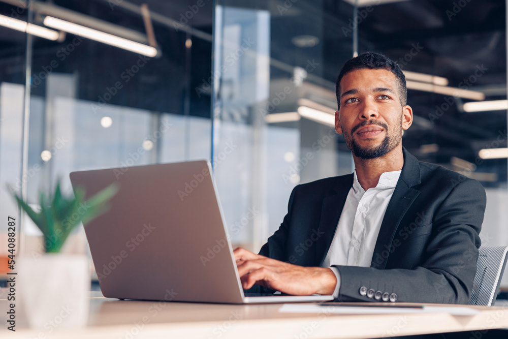 Handsome african businessman working laptop and looking away while sitting in modern office Handsome african businessman working laptop and looking away while sitting in modern office