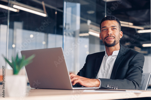 Handsome african businessman working laptop and looking away while sitting in modern office