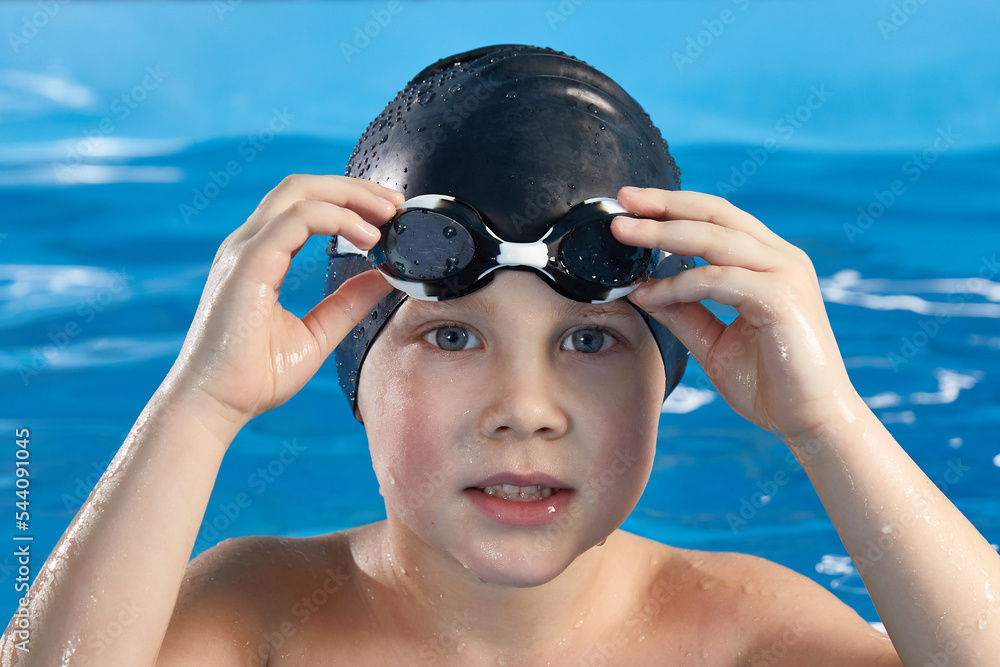 Preschool boy learning how to swim in a pool wearing swimming cap and