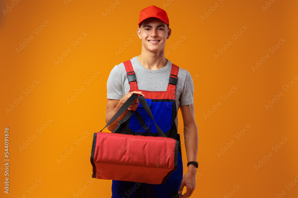 Young courier in uniform with thermo bag on yellow background Young courier in uniform with thermo bag on yellow background