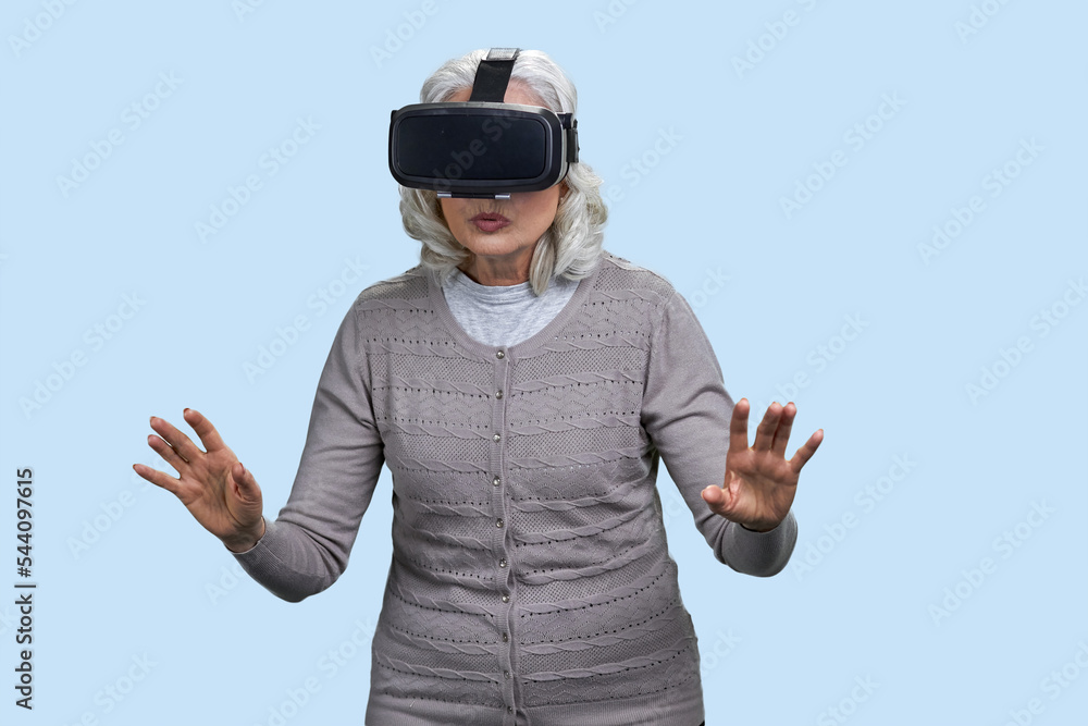 Senior woman with virtual reality headset is shocked by VR experience. Isolated on blue. Senior woman with virtual reality headset is shocked by VR experience. Isolated on blue.