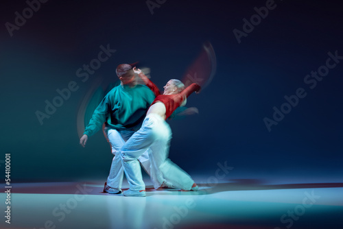 Portrait of young man and woman dancing isolated over dark blue background with mixed lights. Hip-hop performance © Lustre