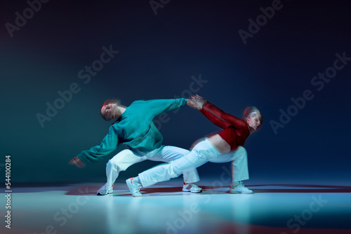 Portrait of young man and woman dancing isolated over dark blue background with mixed lights. Trajectory of movements
