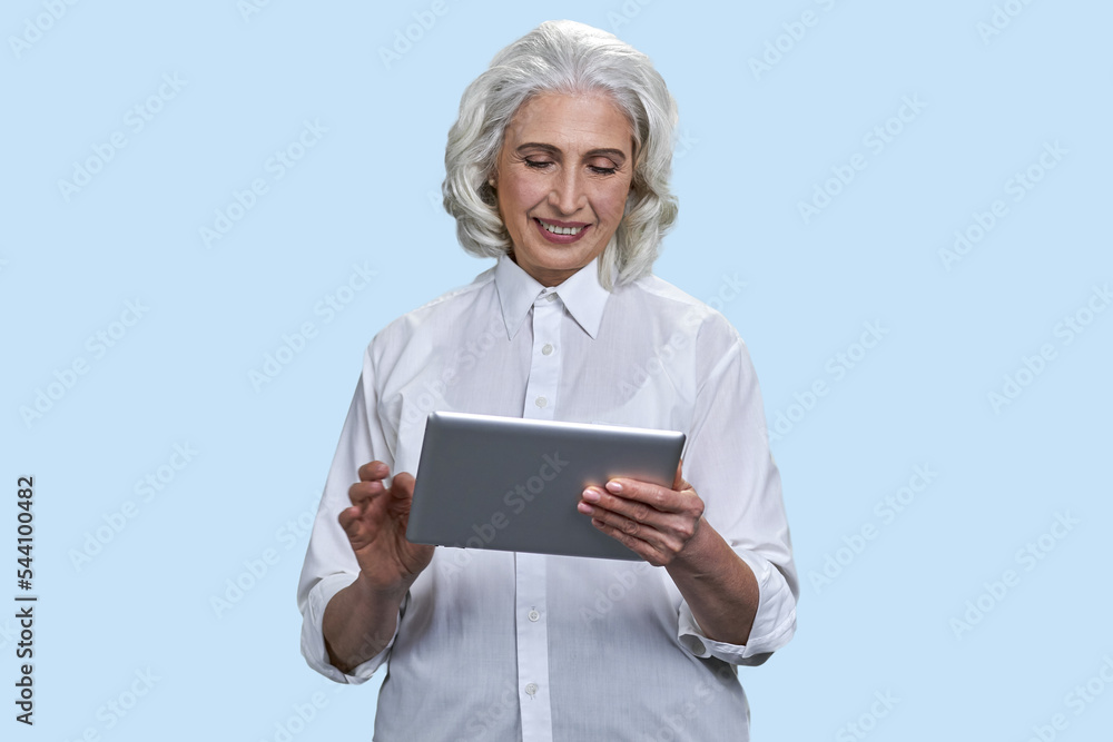 Smiling senior gray-haired woman using tablet pc. Isolated on pale blue background. Smiling senior gray-haired woman using tablet pc. Isolated on pale blue background.