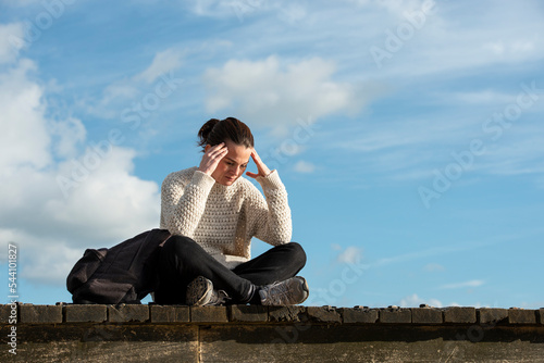 Woman sitting outside with her head in her hand, looking upset or down.