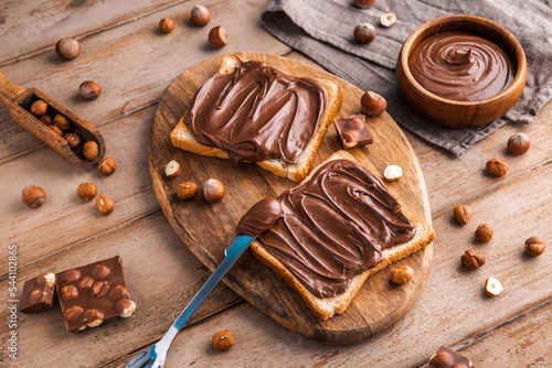 Fotografie, Obraz Board of bread with chocolate paste and hazelnuts on wooden background