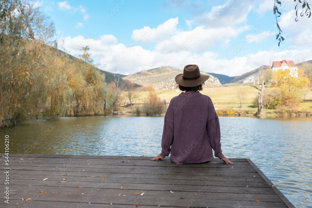 Woman sitting with her back on a wooden bridge looks to the future with a beautiful view of a mountain lake and forest. The concept of relaxation and meditation unity with nature. Woman sitting with her back on a wooden bridge looks to the future with a beautiful view of a mountain lake and forest. The concept of relaxation and meditation unity with nature.