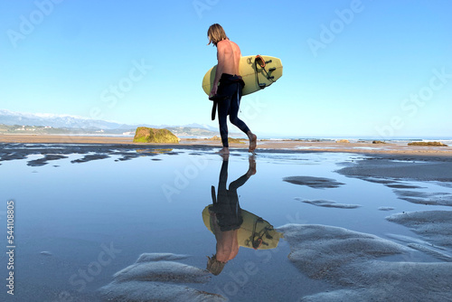 Surfer walking on the quiet beach with a surfboard under his arms