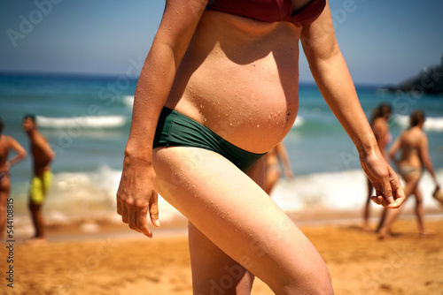 Pregnant woman with a big belly walking on the beach after a swim in the ocean