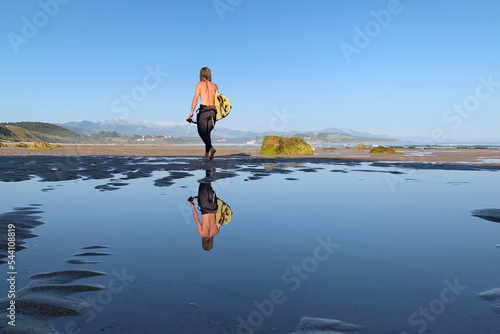 Surfer walking on the quiet beach with a surfboard under his arms